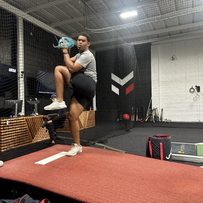 A pitcher at leg lift on the force-plate mound inside the capture cage