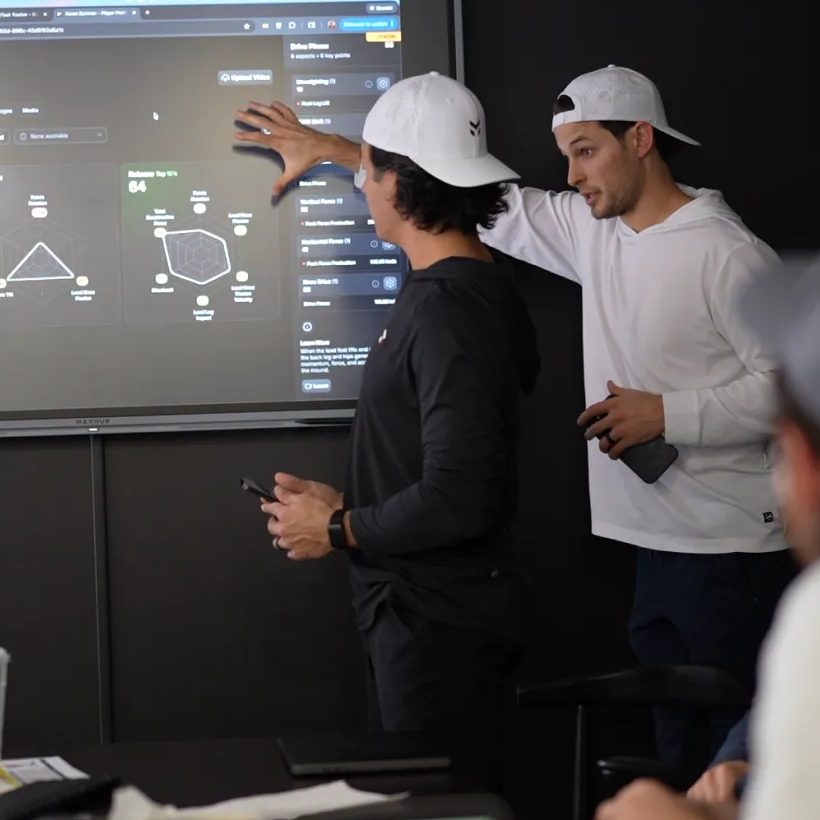 A coach points to an athlete's pillar radar chart on a wall display during a review